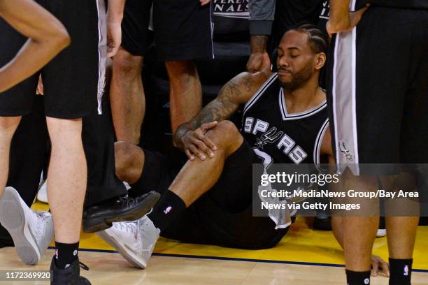 San Antonio Spurs' Kawhi Leonard grabs his leg after suffering an injury while playing against the Golden State Warriors during the third quarter of...