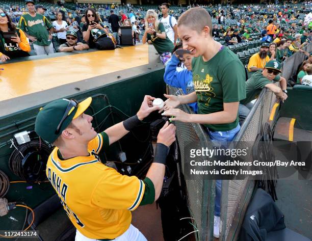 Oakland Athletics outfielder Mark Canha autographs a ball for Megan Pato of Oakley, before the start of the A's baseball game against the Minnesota...