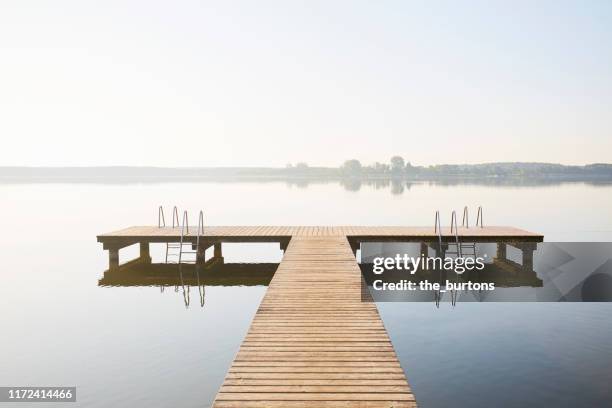 jetty at an idyllic lake with smooth water in the morning against claer sky, tranquil scene - wood pier stock pictures, royalty-free photos & images