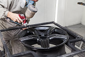 Painting the element body of the car - the aluminum alloy wheel with the help of aerograf in black color by the hand of painter repairman in the industrial professional garage. Auto service industry.
