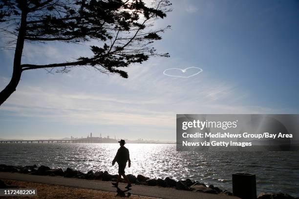 Man walks along the Emeryville Marina as a skywriting airplane draws a heart over the San Francisco Bay on Sunday, Oct. 1 in Emeryville, Calif. The...