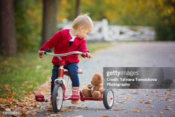 cute little baby girl, riding a tricycle in an autumn park, cute blond toddler girl - tricycle stock pictures, royalty-free photos & images