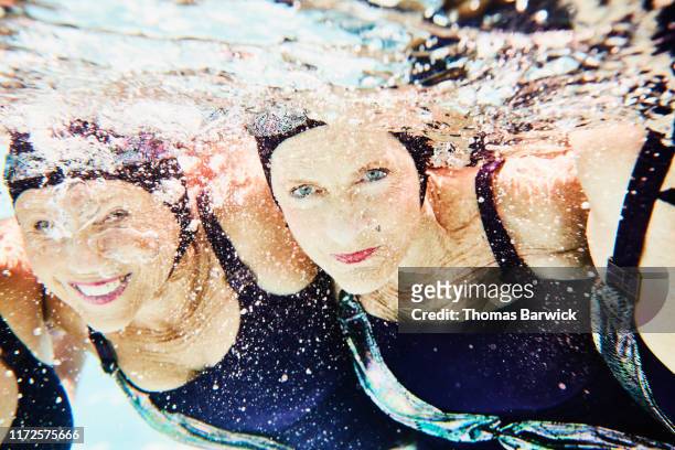 underwater view of smiling senior female synchronized swimmers with arms around each other - athleticism stockfoto's en -beelden