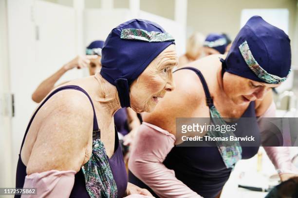 Senior female synchronized swimmer preparing for show in locker room with teammates
