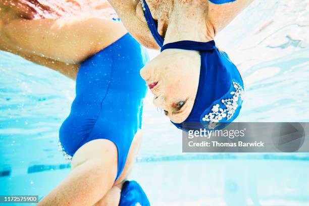 View from underwater of senior female synchronized swimmer upside down underwater during routine