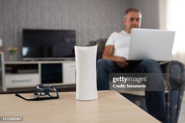 mature man using laptop and virtual assistant at home - coluna inteligente imagens e fotografias de stock