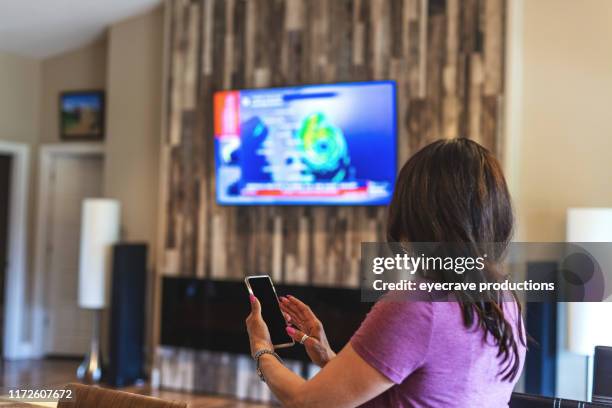 mature adult hispanic female operating smart devices in her home through the use of smart phone in western colorado - smart tv imagens e fotografias de stock