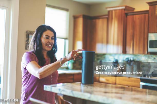 mature adulte hispanique femme opérant dispositifs de haut-parleur intelligents dans sa maison par l'utilisation du téléphone intelligent dans le colorado occidental - haut parleur intelligent photos et images de collection