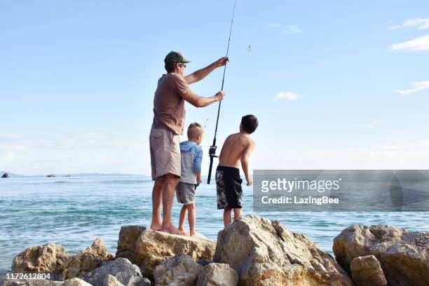 children and father fishing on coastal rocks - new zealand beach stock pictures, royalty-free photos & images