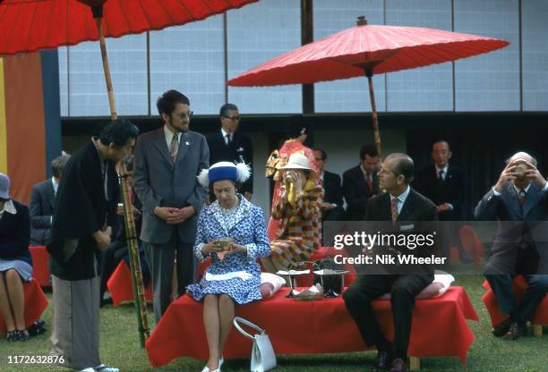 Queen Elizabeth and Prince Philipp sit under umbrellas in grounds of Shinto Temple in Kyoto at tea ceremony during Royal Tour of Japan in 1975.