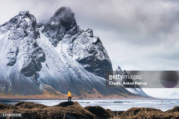 man in a yellow jacket on the background of vestrahorn mountain. iceland - snow on grass stock pictures, royalty-free photos & images
