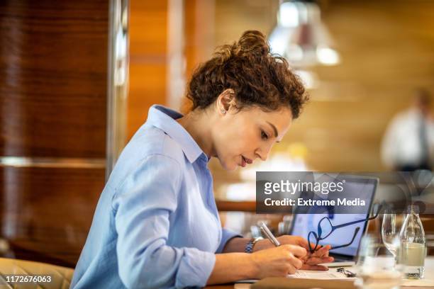 unternehmerin schreibt etwas auf, während sie in einem exklusiven restaurant sitzt - finanzbericht stock-fotos und bilder