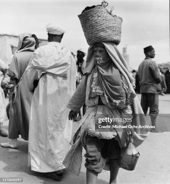 An Amazigh or Berber woman carrying a basket on her head in the Djemaa El Fna market in Marrakesh, Morocco, circa 1950.