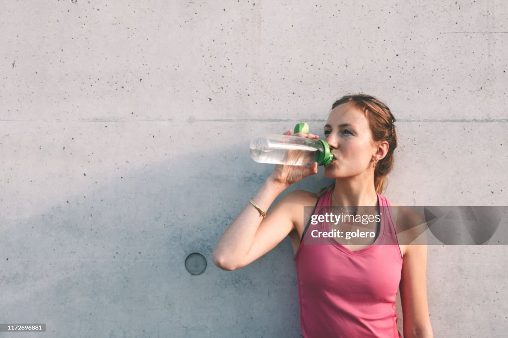 Sportlerin Trinkwasser vor Betonwand