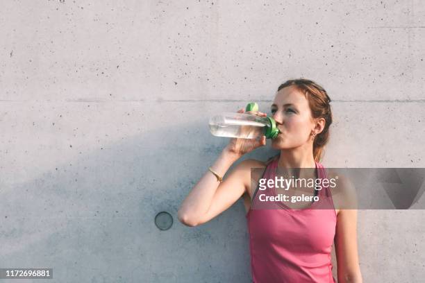 sportvrouw drinkwater voor betonnen muur - urban areas　water front stockfoto's en -beelden