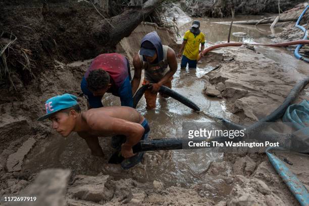 Miners use a high pressure hose to erode river banks in a search for gold in a recently dug mine at the edge of the Canaima National Park in...