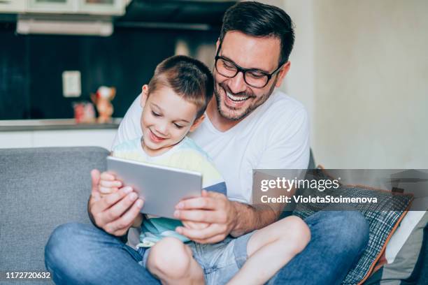 happy father and son looking at digital tablet in the living room - touchpad stock pictures, royalty-free photos & images