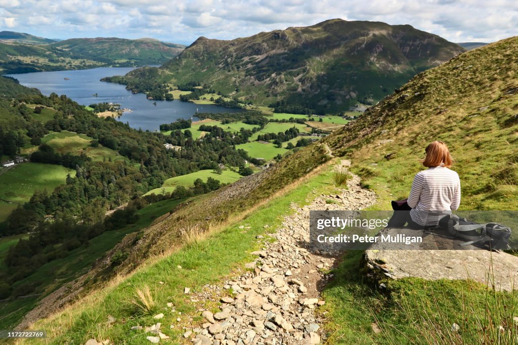 A woman rests on a rock overlooking Ullswater and Patterdale - English Lake District