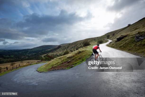 road cyclist climbing hairpin bends up hillside. - hardwork stock pictures, royalty-free photos & images