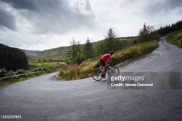 road cyclist climbing hairpin bends up steep road. - uphill stockfoto's en -beelden