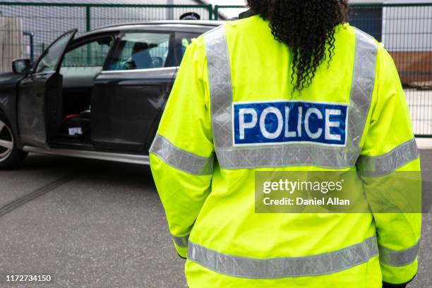 back of police officer wearing high vis police jacket in front of abandoned car - traffic police officer - fotografias e filmes do acervo