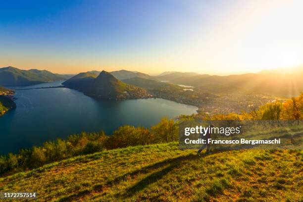 tourist with backpack walks on a path at sunset with view to the city of lugano and lake. monte brè, lugano, canton of ticino, switzerland, europe. - ticino canton 個照片及圖片檔