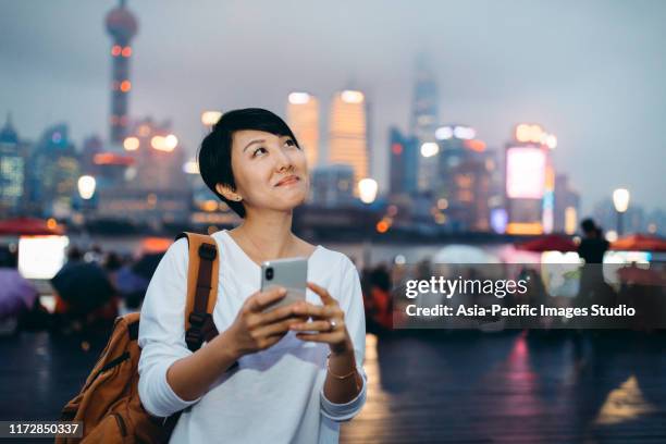 asiatische frau mit handy in der belebten innenstadt, hintergrund ist die finanziellen wolkenkratzer in lujiazui financial district, shanghai, china. - japanese bussiness woman looking up stock-fotos und bilder