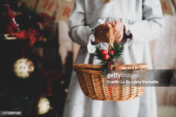 little girl on christmas stage holding a basket next to a christmas tree. - cesta de navidad fotografías e imágenes de stock