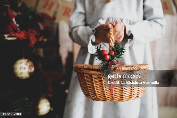 little girl on christmas stage holding a basket next to a christmas tree. - christmas basket stock pictures, royalty-free photos & images
