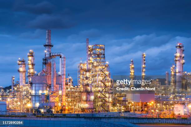 a modern, illuminated refinery is visible at dusk. lights from the buildings and streets glow. - distillation tower stock pictures, royalty-free photos & images