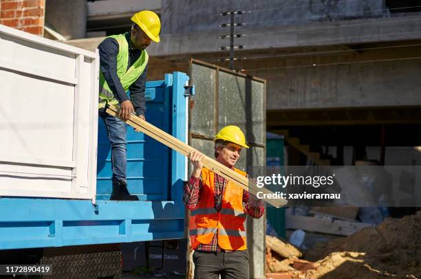 male workers unloading planks from truck at site - construction equipment stock pictures, royalty-free photos & images