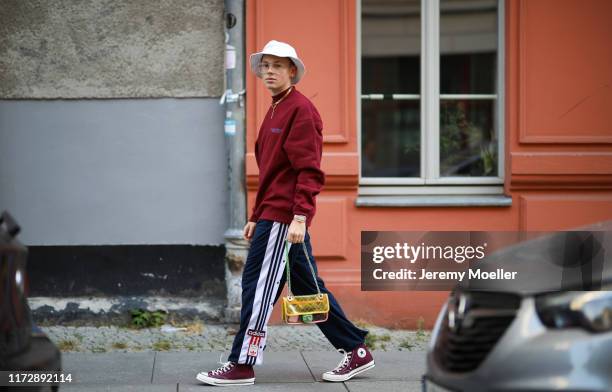 Erik Scholz wearing Converse sneaker, Adidas trackpants, Chanel bag, Daily Paper sweater, Calvin Klein bucket hat and jewelry from Ariane Ernst and...