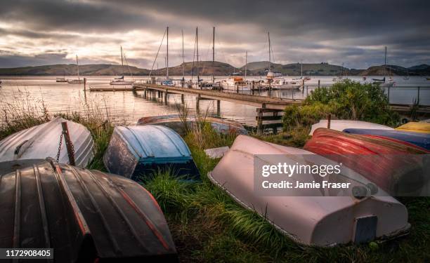deborah bay, dunedin new zealand pier and tender dinghies on moody day - dinghy stock pictures, royalty-free photos & images