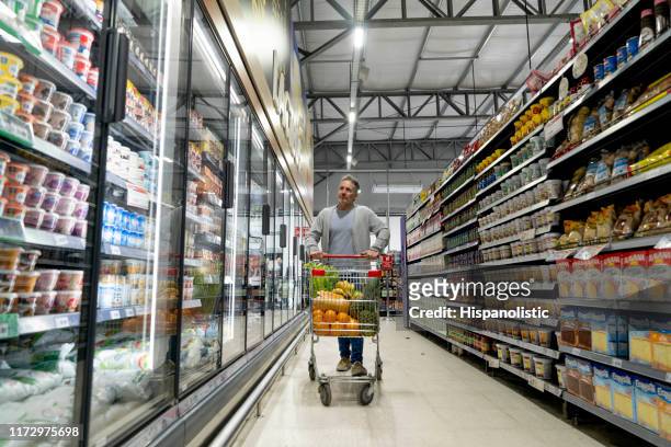拉丁美洲男性顧客推著推車走路，一邊看著超市冷藏區的產品 - 大賣場 個照片及圖片檔