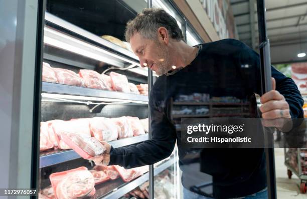 hombre adulto latinoamericano comprando carne en la sección refrigerada de un supermercado - red meat fotografías e imágenes de stock