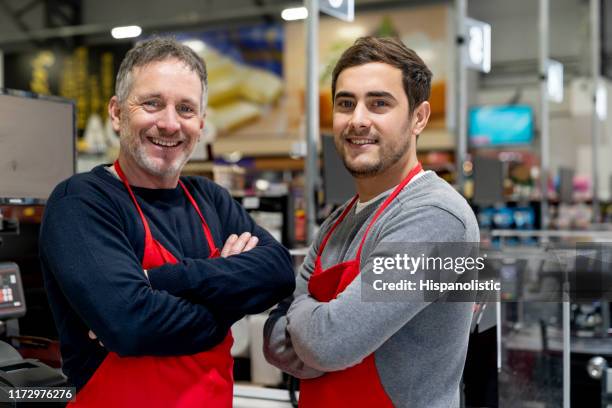 fröhlicher manager und mitarbeiter im supermarkt, der neben der kasse steht und mit gekreuzten armen lächelnd vor der kamera steht - supermarket register stock-fotos und bilder