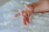 Child's hand with a crucifix on a white cloth background.