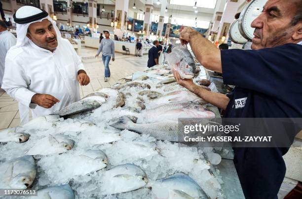 Man buys a zubaidi, or silver pomfret , fish from a seller at a fish market in Kuwait City Octpober 2, 2019.