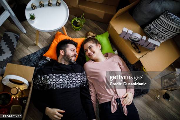 couple lying on floor by open boxes in new home smiling - couple seated apartment hipster imagens e fotografias de stock