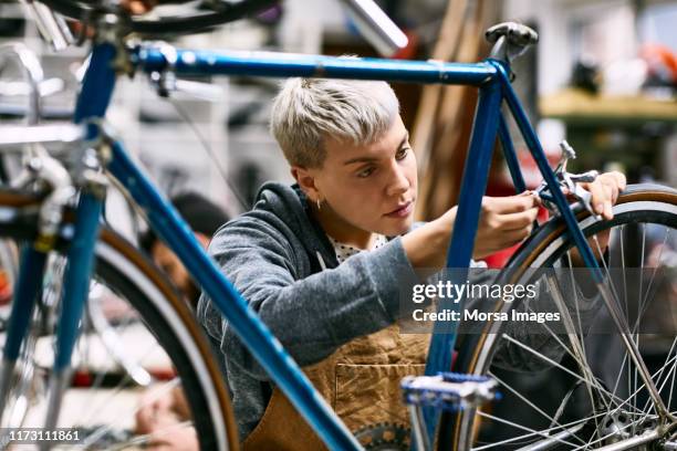 joven empleada reparando el freno de la bicicleta - reparar fotografías e imágenes de stock
