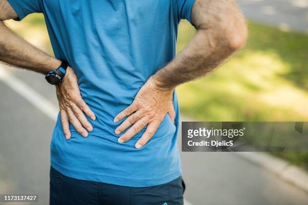 sporty senior man having a back pain close up. - backache stock pictures, royalty-free photos & images