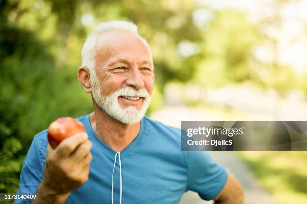 happy sporty senior man take care of his health. eating an apple. - apple fruit stock pictures, royalty-free photos & images