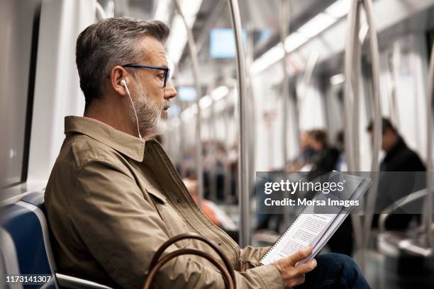 mature man reading book in subway train - transportation hearing stock-fotos und bilder