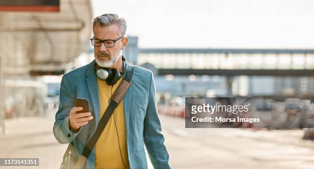 man using mobile phone while walking on sidewalk - veste homme photos et images de collection