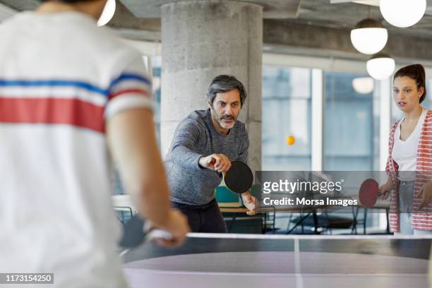 compañeros de trabajo jugando al tenis de mesa en la oficina - table tennis fotografías e imágenes de stock