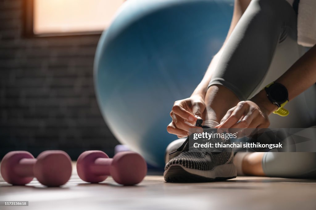 Young sporty woman with smart watch tying shoelaces in fitness