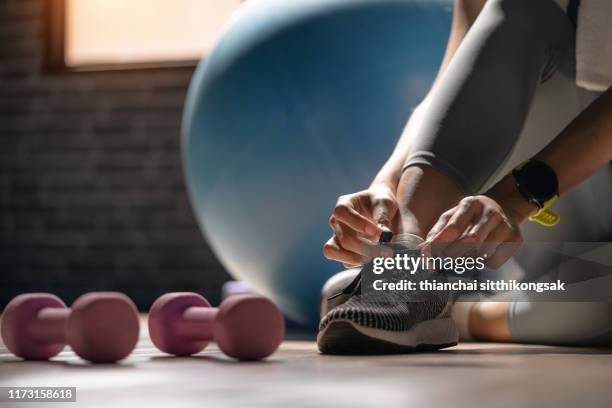 young sporty woman with smart watch tying shoelaces in fitness - poids-et-haltères photos et images de collection