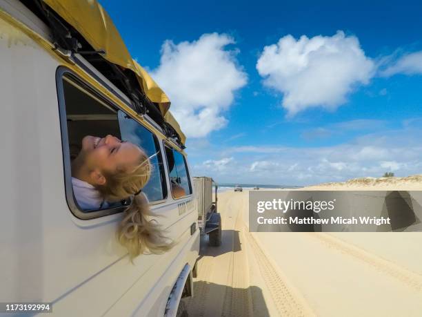 a girl sticks her head out the window as she drives down the beach. - explore australia foto e immagini stock