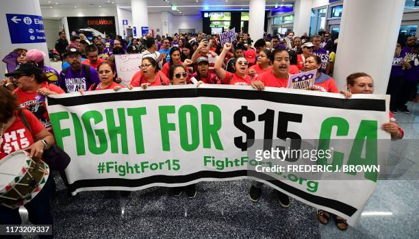 Banner for a $15 dollar per hour minimum wage is displayed as airport employees are joined by drivers from Uber and Lyft and other southern...