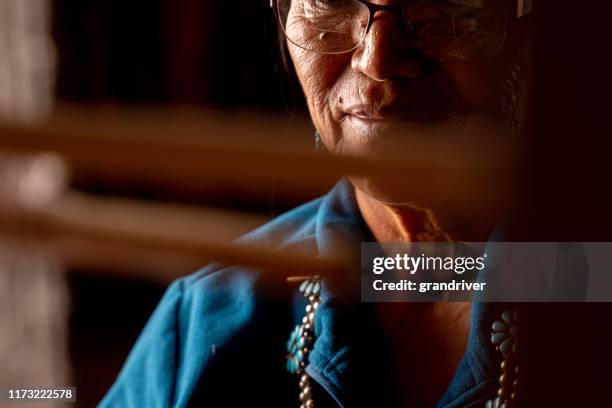 senior native american navajo vrouw zittend in een traditionele authentieke hogan met behulp van een zelfgemaakte loom om een handgeweven deken te maken - cherokee indian women stockfoto's en -beelden